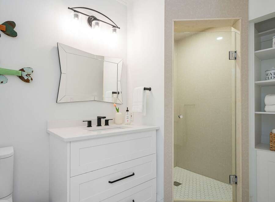 This modern bathroom features a sleek white vanity with a black faucet and a large, uniquely shaped mirror.