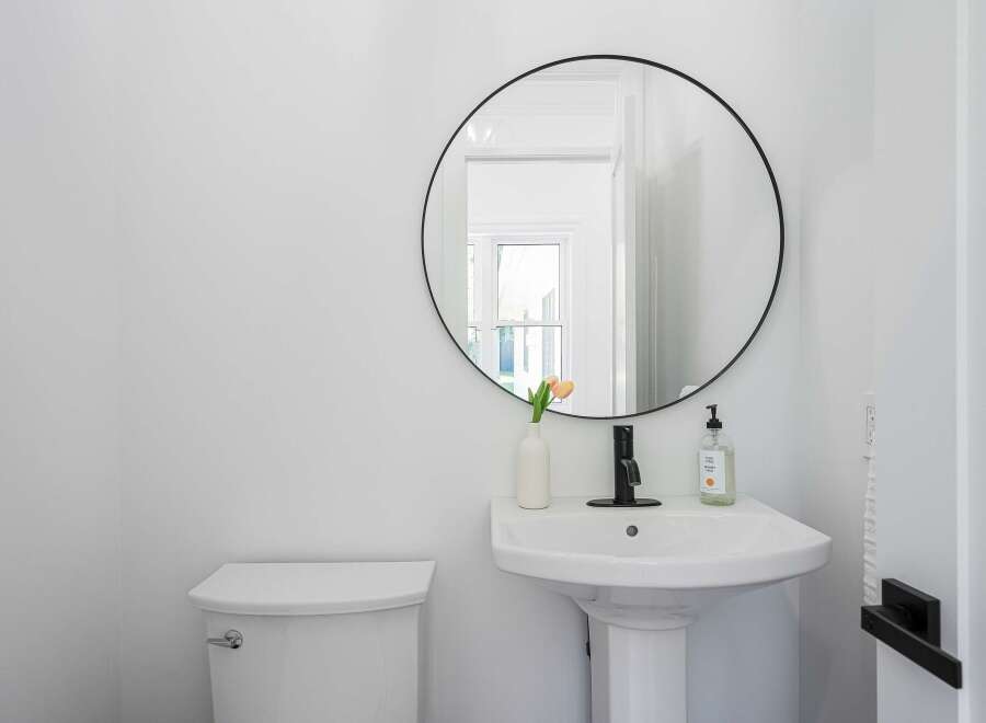 This modern bathroom features a sleek white pedestal sink with a black faucet, complemented by a round black-framed mirror.