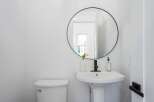 This modern bathroom features a sleek white pedestal sink with a black faucet, complemented by a round black-framed mirror.