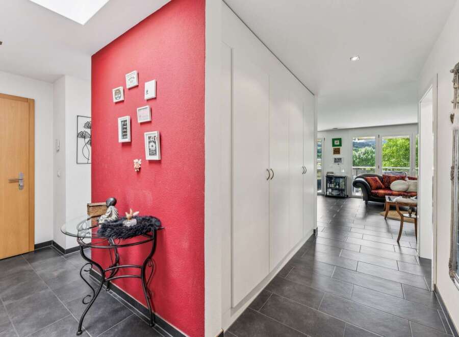 Step into this inviting hallway featuring a vibrant red accent wall adorned with a collection of framed pictures, creating a warm and personal touch.