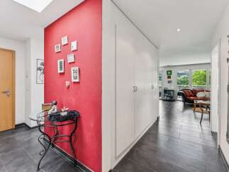 Step into this inviting hallway featuring a vibrant red accent wall adorned with a collection of framed pictures, creating a warm and personal touch.