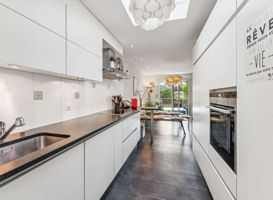 This modern kitchen features sleek white cabinetry and a dark granite countertop, complemented by a stainless steel sink and faucet.