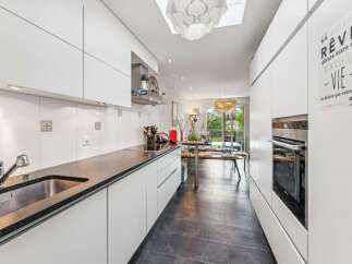 This modern kitchen features sleek white cabinetry and a dark granite countertop, complemented by a stainless steel sink and faucet.