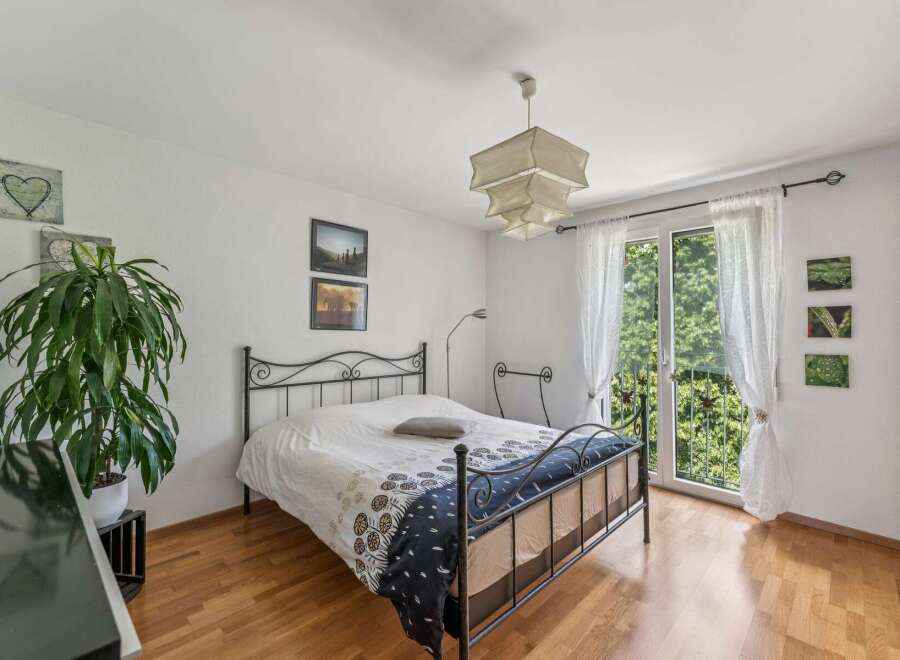This charming bedroom features a comfortable bed with a decorative duvet and a metal frame, complemented by a large potted plant and tasteful wall art.