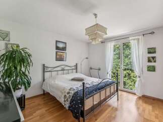 This charming bedroom features a comfortable bed with a decorative duvet and a metal frame, complemented by a large potted plant and tasteful wall art.