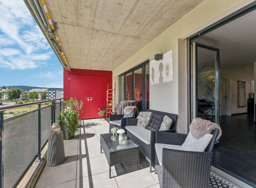 Enjoy outdoor living on this spacious balcony featuring comfortable wicker furniture and a glass-top coffee table, perfect for relaxing or entertaining.