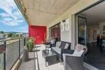 Enjoy outdoor living on this spacious balcony featuring comfortable wicker furniture and a glass-top coffee table, perfect for relaxing or entertaining.