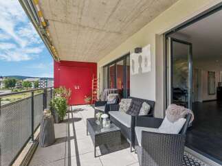 Enjoy outdoor living on this spacious balcony featuring comfortable wicker furniture and a glass-top coffee table, perfect for relaxing or entertaining.
