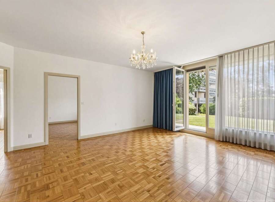 Step into this elegant living space featuring gleaming parquet flooring that reflects the natural light pouring in from the large glass doors.