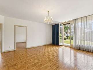Step into this elegant living space featuring gleaming parquet flooring that reflects the natural light pouring in from the large glass doors.