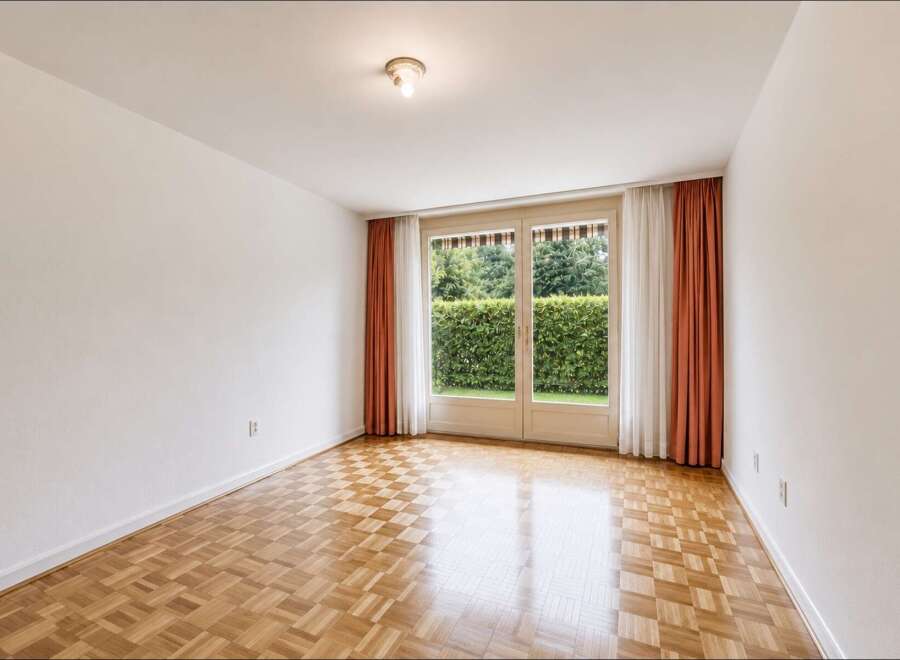This empty room features a beautiful parquet floor that reflects the natural light streaming in from the large double doors.