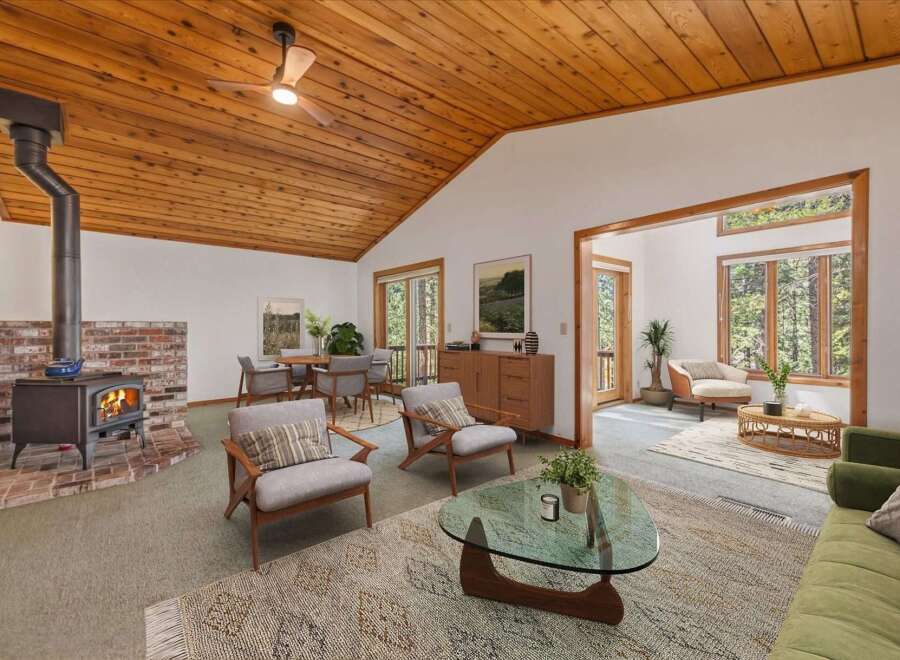 Experience cozy living in this charming home featuring a rustic wood-burning fireplace and a vaulted wood-paneled ceiling with a ceiling fan.