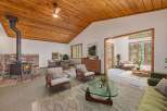 Experience cozy living in this charming home featuring a rustic wood-burning fireplace and a vaulted wood-paneled ceiling with a ceiling fan.