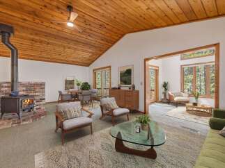 Experience cozy living in this charming home featuring a rustic wood-burning fireplace and a vaulted wood-paneled ceiling with a ceiling fan.