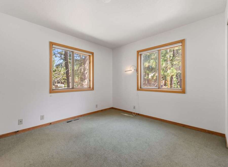 This bedroom offers a serene retreat with two large windows framing picturesque forest views.