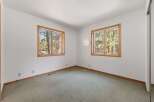 This bedroom offers a serene retreat with two large windows framing picturesque forest views.