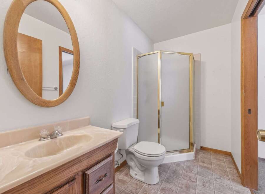 This bathroom features a vanity with a marble countertop and a wooden cabinet base, complemented by an oval wooden-framed mirror.