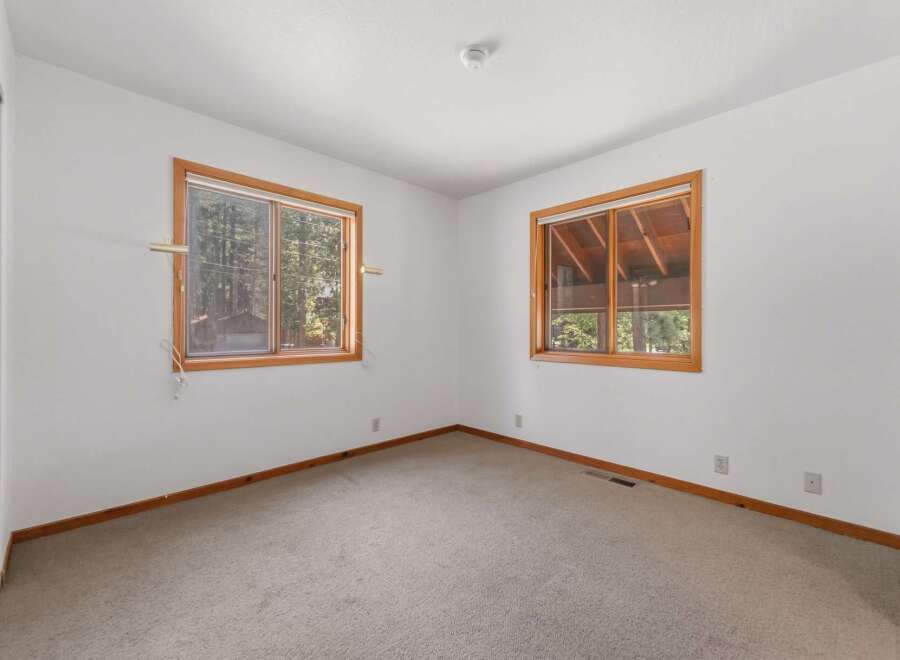 This bright and airy bedroom features two large windows that flood the space with natural light and offer serene views of the surrounding trees.