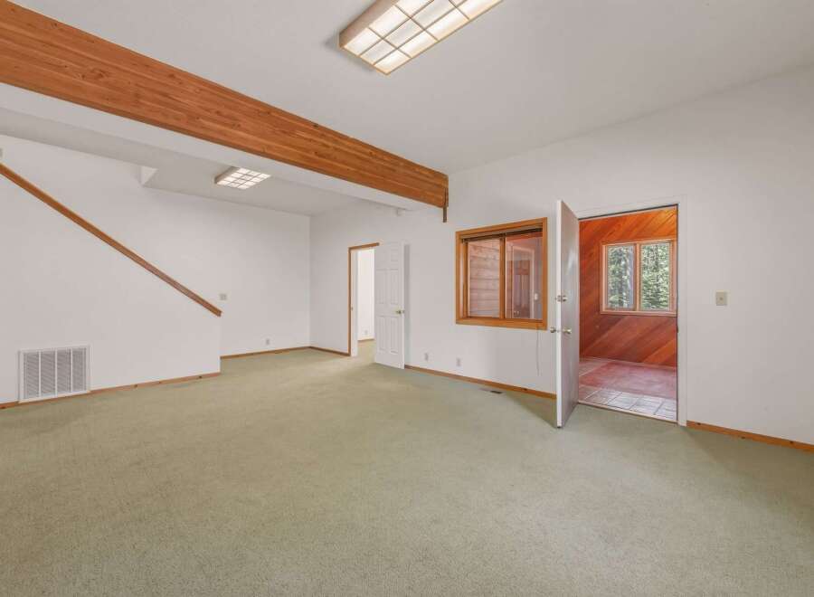 Step into this spacious living area featuring a charming wooden beam accent and a cozy, carpeted floor.