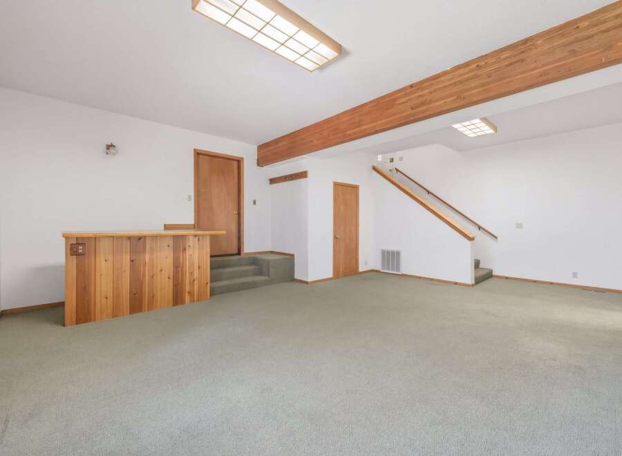 Discover this spacious basement living area featuring a charming wooden bar, perfect for entertaining guests.
