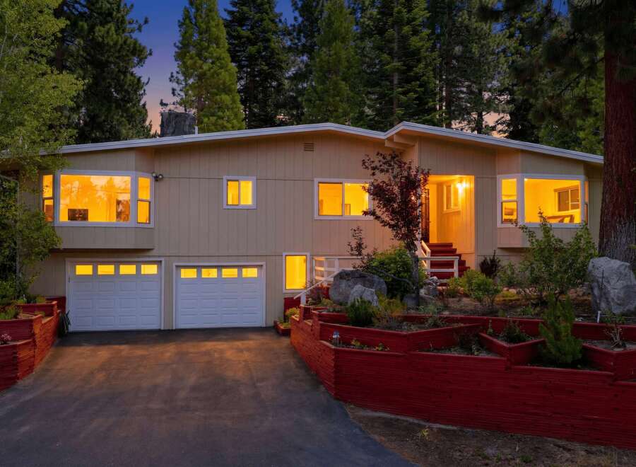 Nestled amidst tall pine trees, this charming home offers a warm and inviting ambiance, especially as dusk settles.