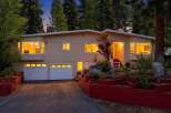 Nestled amidst tall pine trees, this charming home offers a warm and inviting ambiance, especially as dusk settles.