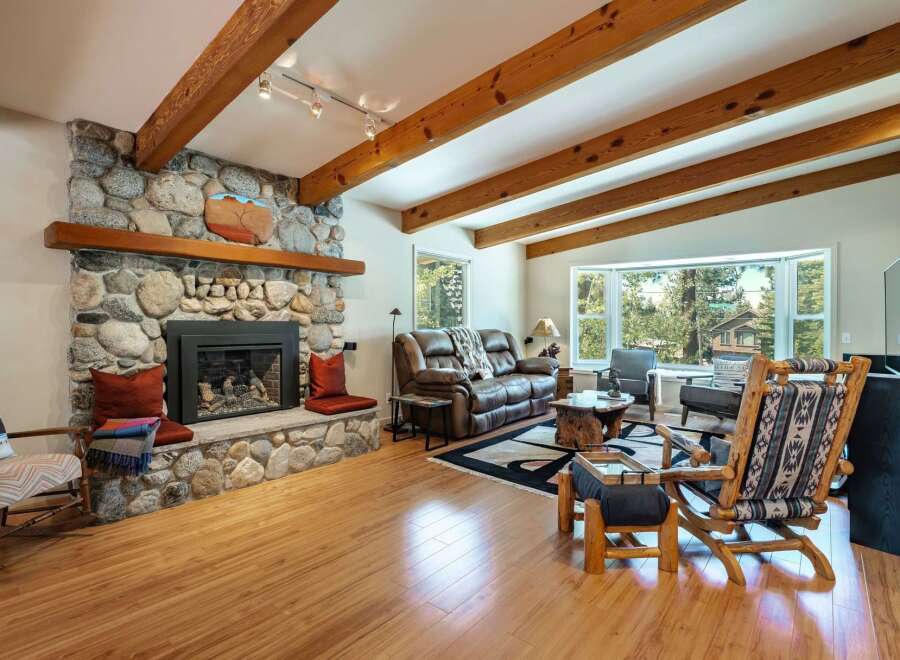 Experience rustic charm in this inviting living room, featuring a grand stone fireplace and exposed wooden beams that add warmth and character.