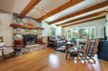 Experience rustic charm in this inviting living room, featuring a grand stone fireplace and exposed wooden beams that add warmth and character.