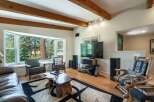 Experience cozy living in this inviting living room, featuring a large bay window with stunning forest views and exposed wooden beams on the ceiling.