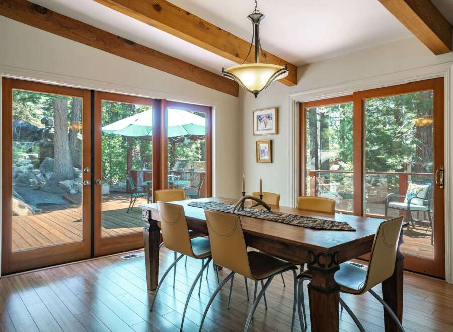 Experience seamless indoor-outdoor living in this stunning dining room, featuring expansive glass doors that open onto a private deck surrounded by lush trees.