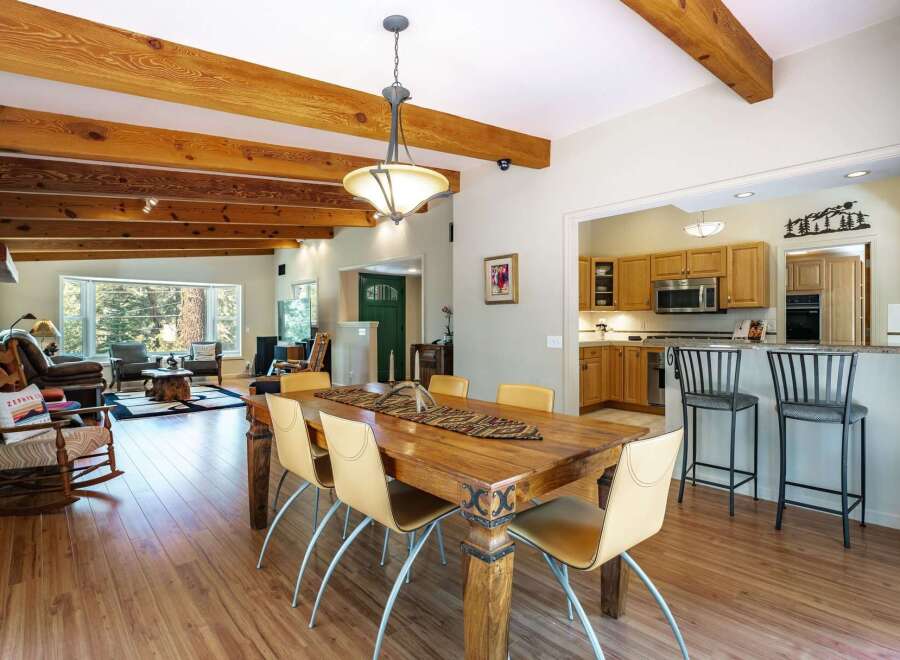 Experience rustic charm and modern comfort in this spacious open-concept living area, featuring exposed wooden beams and a cozy stone fireplace.