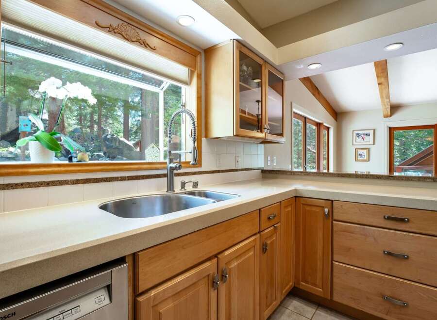 This spacious kitchen boasts a large sink area with a stunning view of the surrounding forest through a wide window.