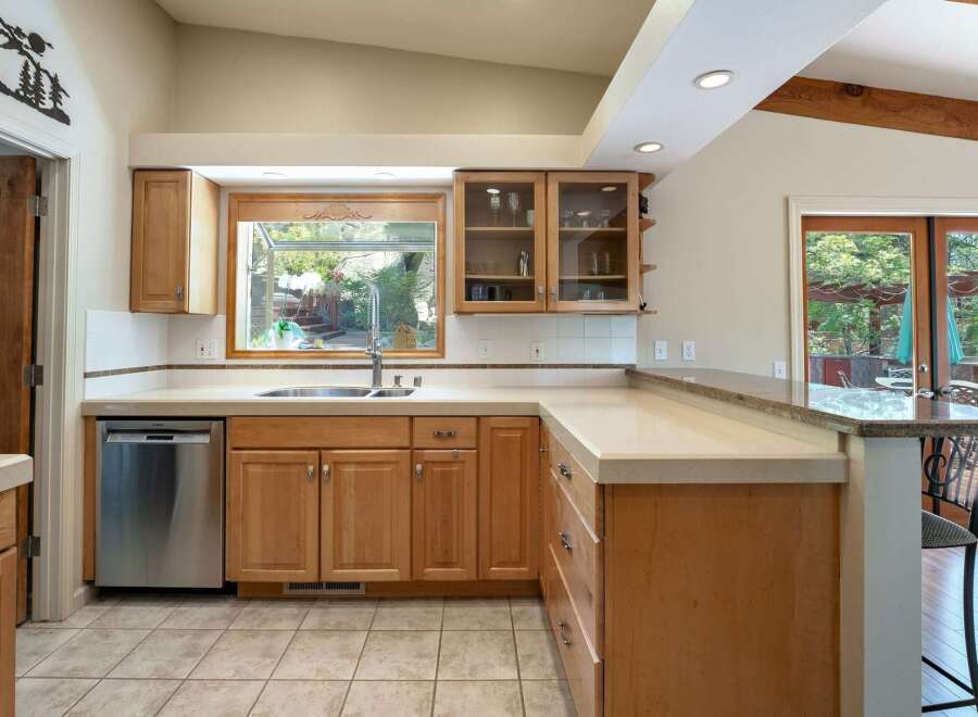 This spacious kitchen boasts ample natural light streaming through a large window above the sink, complemented by elegant wood cabinetry and a sleek granite countertop.