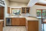 This spacious kitchen boasts ample natural light streaming through a large window above the sink, complemented by elegant wood cabinetry and a sleek granite countertop.