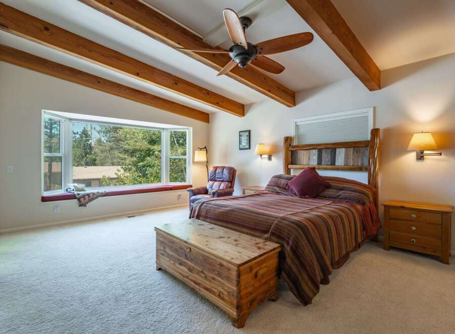 Experience rustic charm in this inviting bedroom featuring exposed wooden beams and a spacious bay window with a built-in seating area, perfect for enjoying the scenic views.