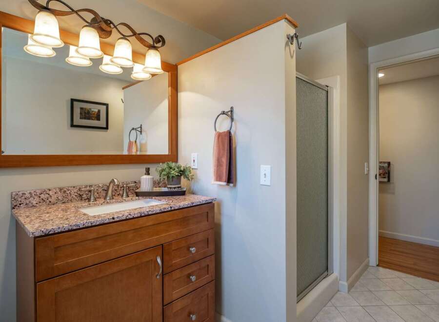 This bathroom features a spacious vanity with a granite countertop and a wooden cabinet, complemented by a large mirror with an ornate light fixture.