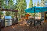 Enjoy outdoor living at its finest on this spacious wooden deck, complete with a built-in stainless steel grill and a large turquoise umbrella providing shade over a dining set.