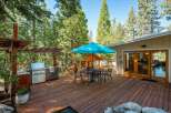 Enjoy outdoor living at its finest on this spacious wooden deck, complete with a built-in grill station and a charming dining set under a vibrant blue umbrella.