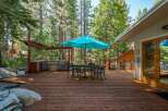 Enjoy outdoor living at its finest on this expansive wooden deck, complete with a built-in outdoor kitchen and a charming dining set under a vibrant turquoise umbrella.