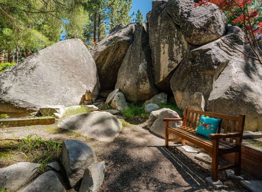 Discover a unique outdoor oasis featuring a charming wooden bench adorned with a decorative pillow, nestled amongst majestic boulders.