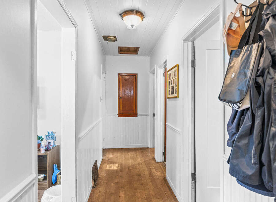 Step into this charming hallway featuring a warm wooden floor and beadboard wainscoting, creating a cozy and inviting atmosphere.