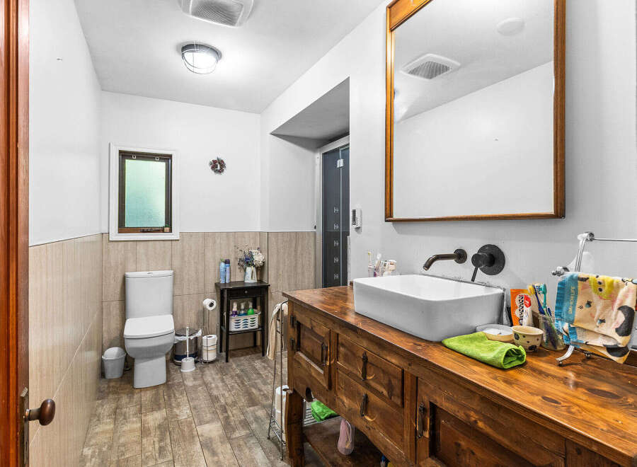 This charming bathroom features a rustic wooden vanity with a vessel sink, complemented by a dark bronze faucet.
