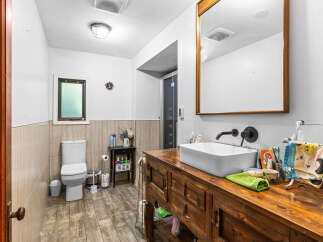 This charming bathroom features a rustic wooden vanity with a vessel sink, complemented by a dark bronze faucet.