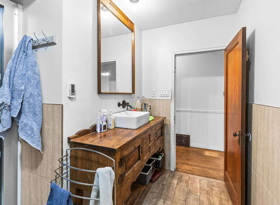 This charming bathroom features a rustic wooden vanity with a modern vessel sink, complemented by a large wooden-framed mirror.