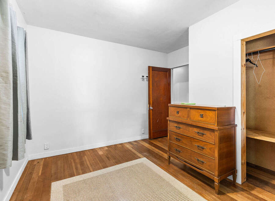 Discover this charming bedroom featuring a classic wooden dresser and a convenient closet with shelving.