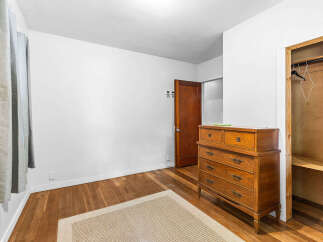 Discover this charming bedroom featuring a classic wooden dresser and a convenient closet with shelving.
