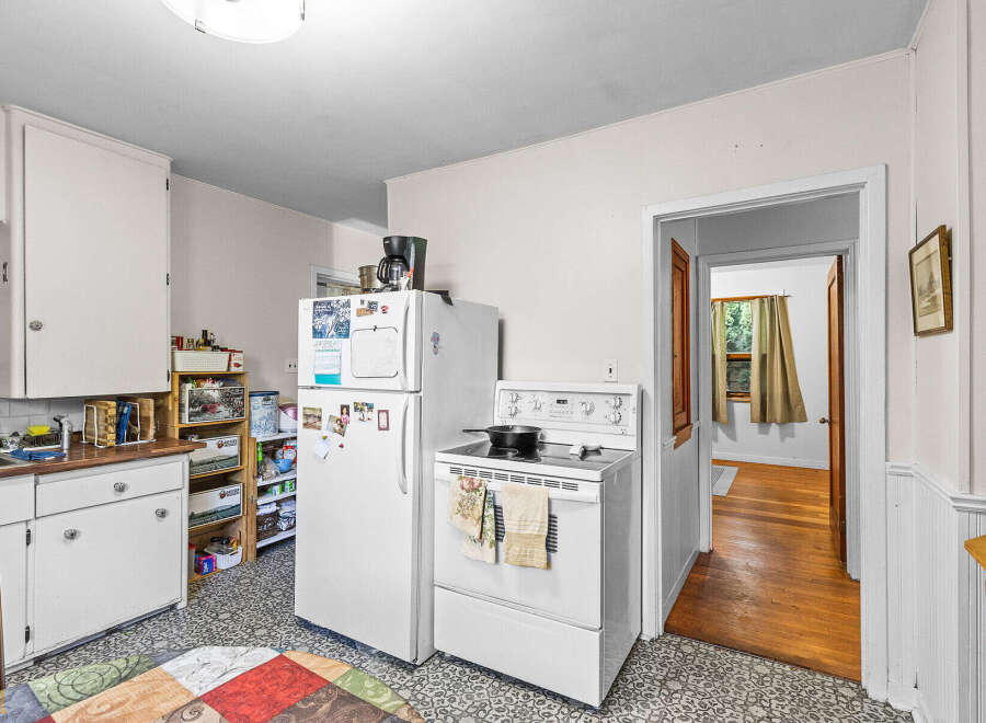 Discover this charming kitchen featuring white appliances, including a refrigerator and a stove with a stovetop pan.