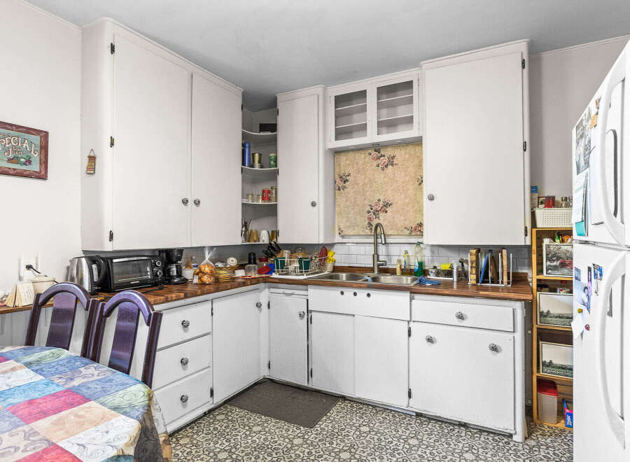 Discover a charming kitchen featuring ample white cabinetry for storage and a cozy dining nook with a colorful quilt-patterned tablecloth.