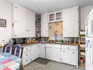 Discover a charming kitchen featuring ample white cabinetry for storage and a cozy dining nook with a colorful quilt-patterned tablecloth.