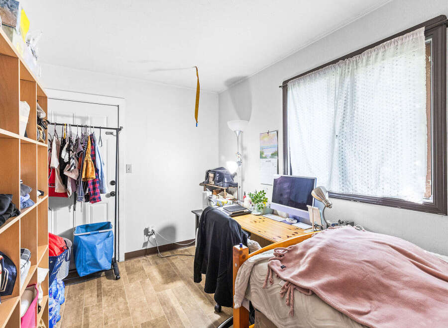 This cozy room features a functional desk area with a computer and ample storage solutions, including a large shelving unit and a clothing rack.